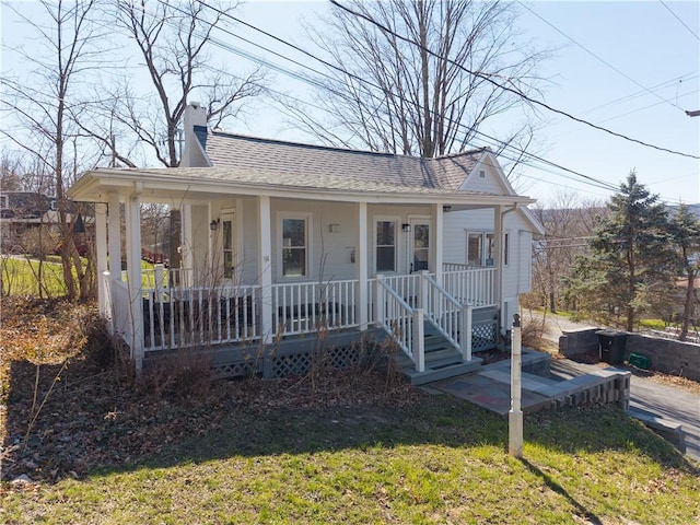 view of front facade featuring a front lawn, roof with shingles, a chimney, and covered porch