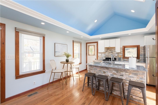 kitchen with white cabinets, a breakfast bar, freestanding refrigerator, and a sink