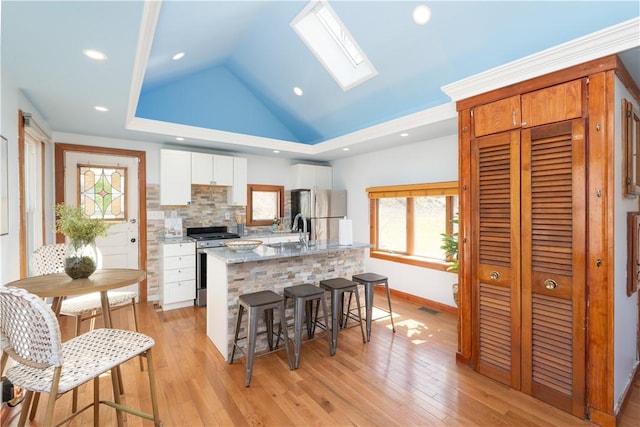 kitchen featuring a kitchen island with sink, white cabinetry, vaulted ceiling with skylight, decorative backsplash, and appliances with stainless steel finishes