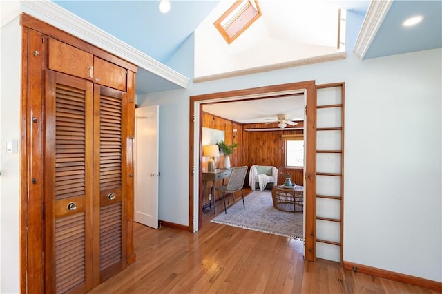 corridor featuring baseboards, vaulted ceiling with skylight, and light wood finished floors