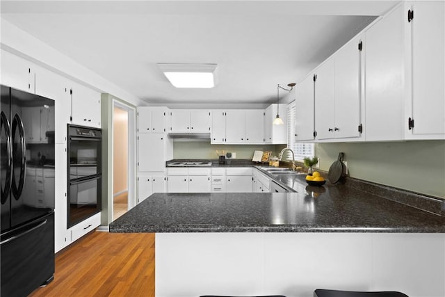 kitchen featuring white cabinets, wood finished floors, a sink, black appliances, and a peninsula