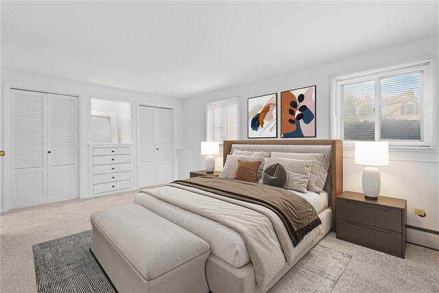 bedroom featuring light colored carpet and multiple closets