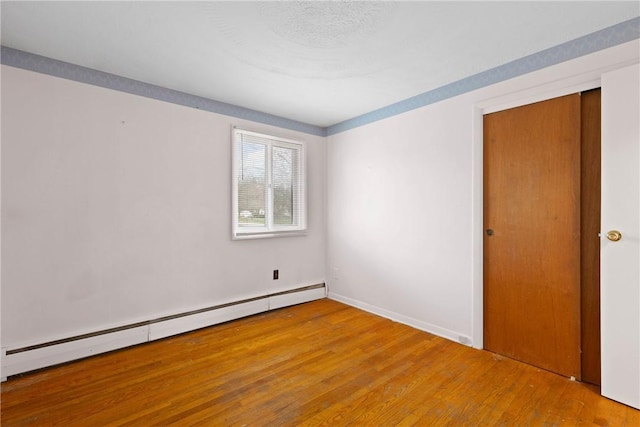 spare room featuring baseboard heating, baseboards, and wood finished floors