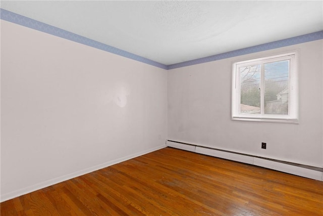 spare room featuring a baseboard heating unit, wood finished floors, and baseboards