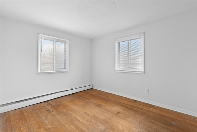 unfurnished room featuring baseboard heating, baseboards, a healthy amount of sunlight, and hardwood / wood-style floors