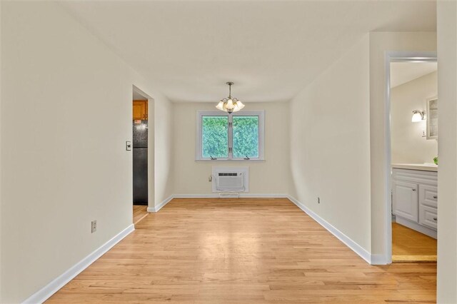 unfurnished dining area featuring baseboards, a notable chandelier, light wood finished floors, and a wall mounted AC