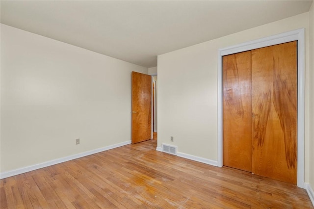 unfurnished bedroom with a closet, light wood-style floors, visible vents, and baseboards