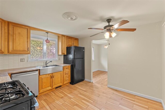 kitchen with a sink, black appliances, decorative backsplash, light countertops, and baseboards