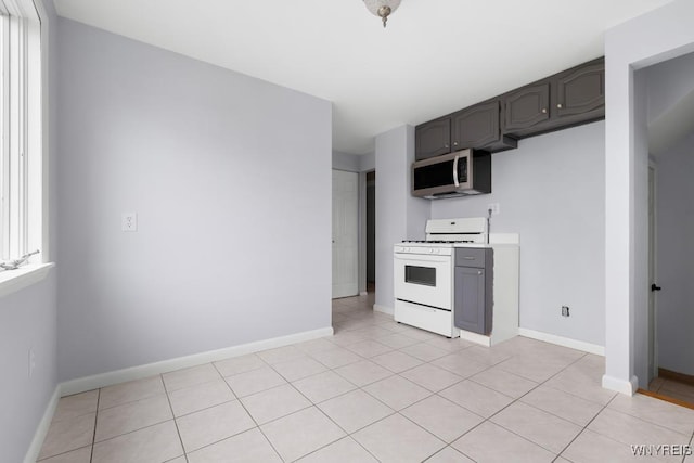 kitchen featuring light countertops, white range with gas stovetop, stainless steel microwave, light tile patterned flooring, and baseboards