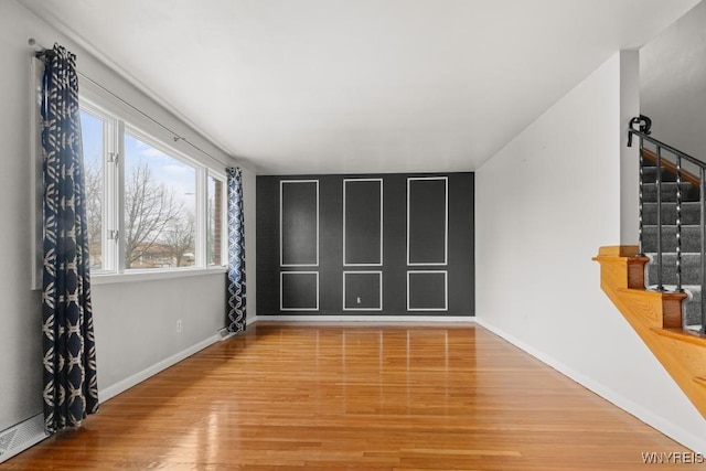 empty room with baseboards, wood finished floors, and stairs