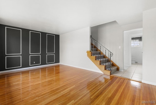 unfurnished living room with baseboards, wood finished floors, and stairway