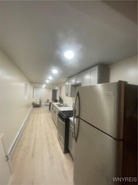 kitchen with a sink, light wood finished floors, white cabinets, appliances with stainless steel finishes, and recessed lighting