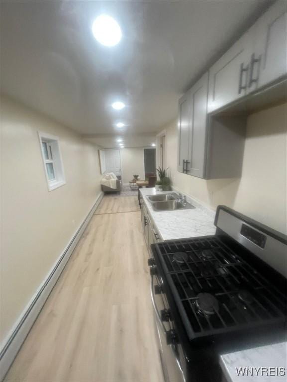 kitchen featuring stainless steel range with gas cooktop, light wood-style flooring, a sink, baseboards, and light countertops