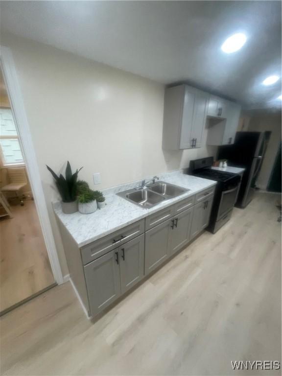 kitchen with light wood-type flooring, a sink, black gas range oven, and gray cabinets