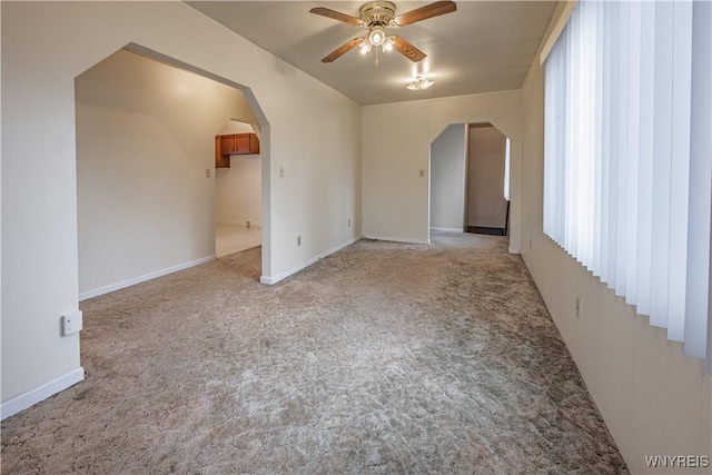 spare room featuring light colored carpet, arched walkways, a ceiling fan, and baseboards