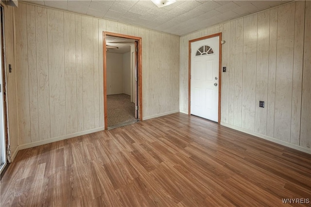 unfurnished room featuring wooden walls, wood finished floors, and baseboards