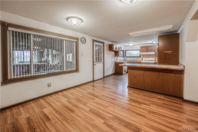 kitchen with stainless steel range with electric cooktop, under cabinet range hood, light wood-type flooring, a peninsula, and brown cabinetry