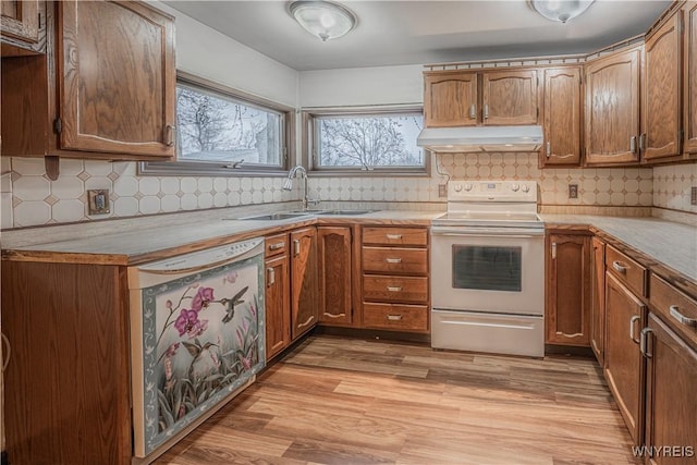 kitchen featuring light wood finished floors, under cabinet range hood, light countertops, a sink, and white appliances