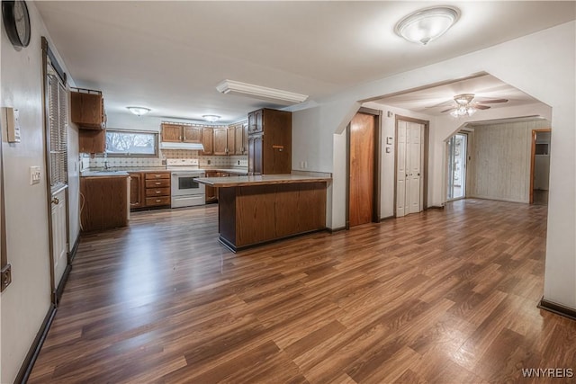 kitchen with white range with electric cooktop, a ceiling fan, open floor plan, a peninsula, and dark wood-style floors