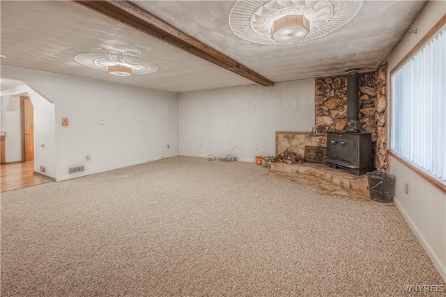 unfurnished living room featuring carpet floors, a wood stove, visible vents, and baseboards