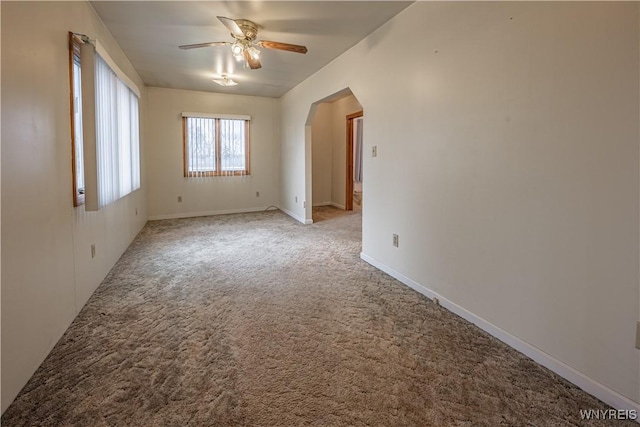 empty room with arched walkways, a ceiling fan, baseboards, and light carpet