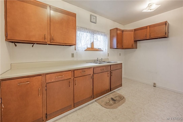 kitchen with a sink, brown cabinetry, light floors, light countertops, and baseboards
