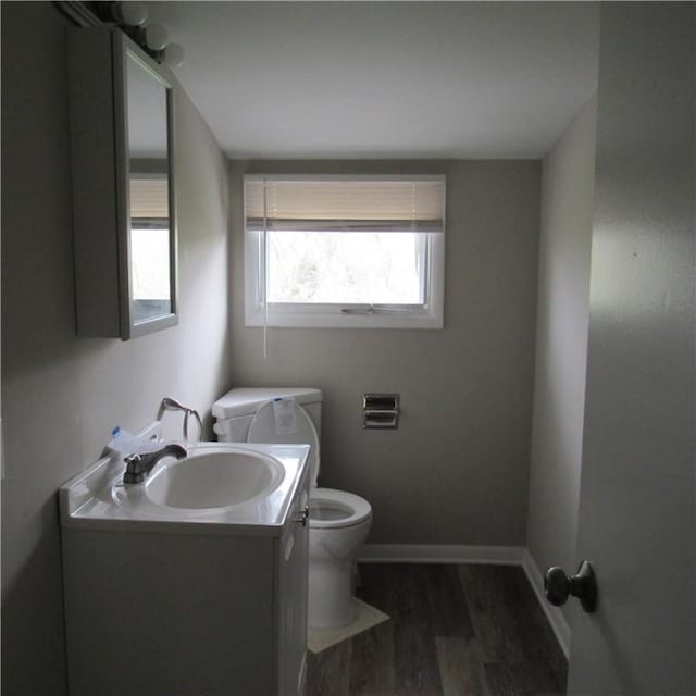 half bath with toilet, vanity, wood finished floors, and baseboards