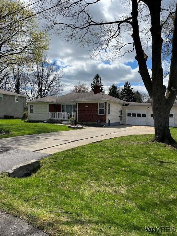 single story home featuring a chimney, a front lawn, driveway, covered porch, and a garage