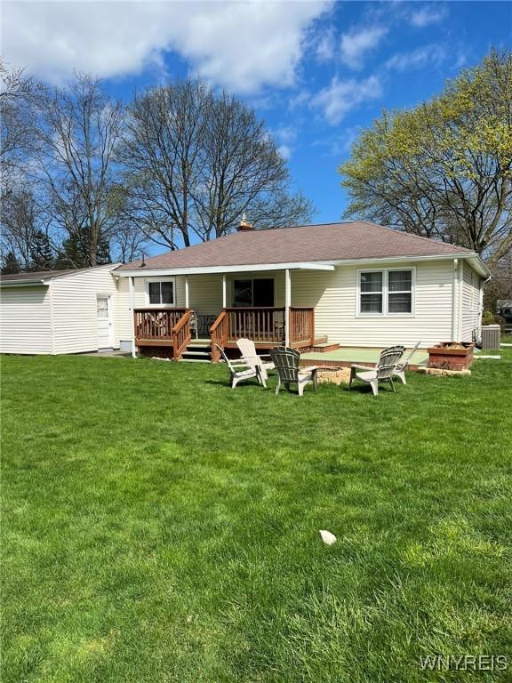 back of property featuring a fire pit, a yard, cooling unit, and a deck