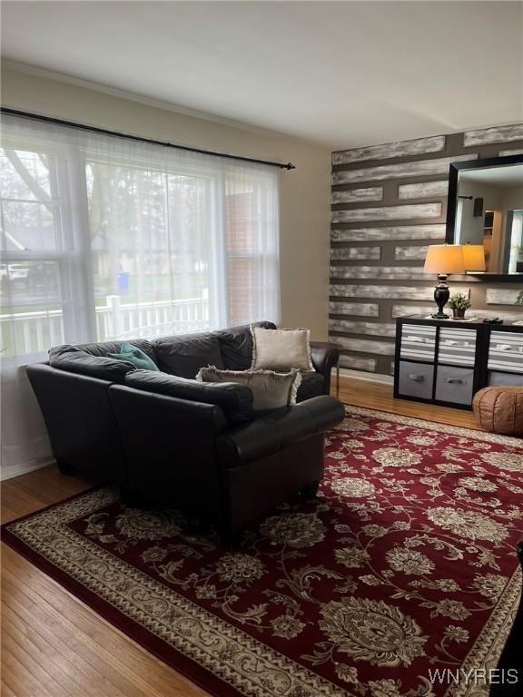 living area with baseboards, an accent wall, and wood finished floors