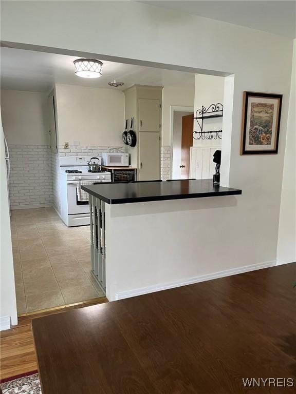 kitchen featuring a peninsula, dark countertops, white appliances, and light wood-type flooring