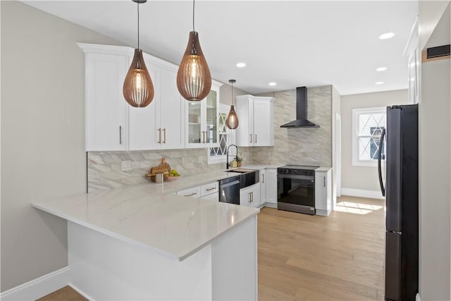 kitchen featuring a sink, wall chimney exhaust hood, decorative backsplash, a peninsula, and appliances with stainless steel finishes