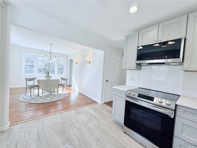 kitchen featuring light wood finished floors, stainless steel appliances, baseboards, decorative backsplash, and light countertops