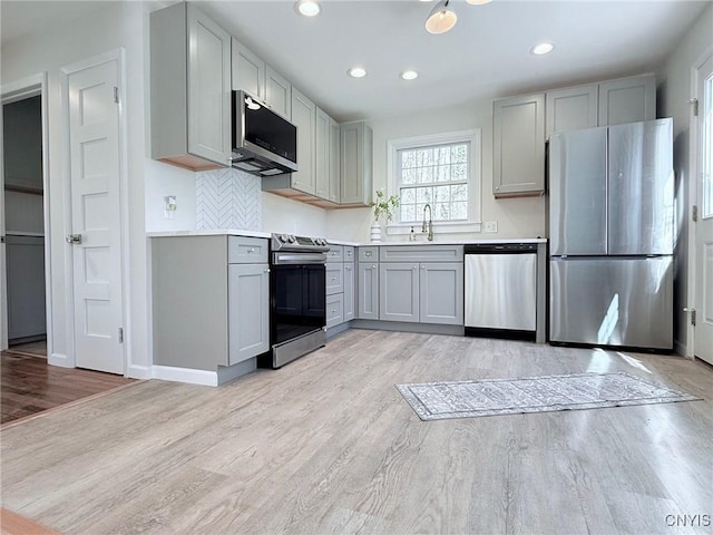 kitchen with light wood-style floors, gray cabinets, stainless steel appliances, and a sink