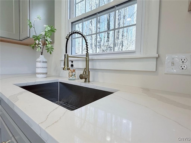 room details with light stone countertops, gray cabinets, and a sink