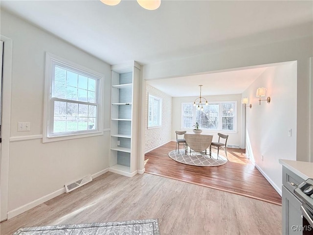 dining area featuring a notable chandelier, a healthy amount of sunlight, visible vents, and light wood-style flooring