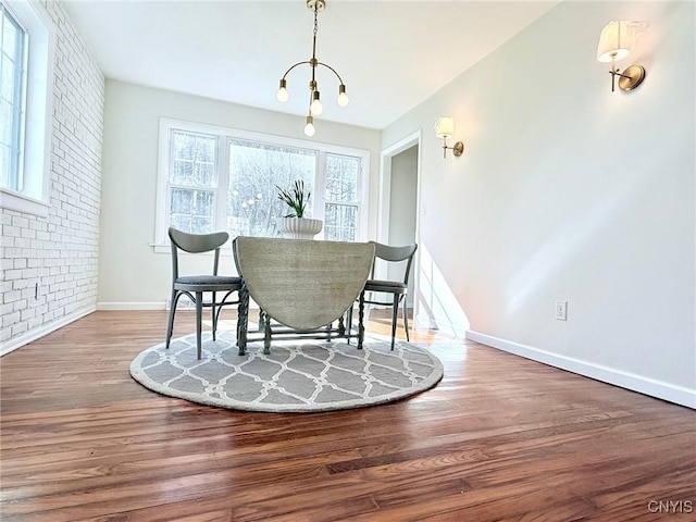 dining space with baseboards, wood finished floors, brick wall, and a chandelier