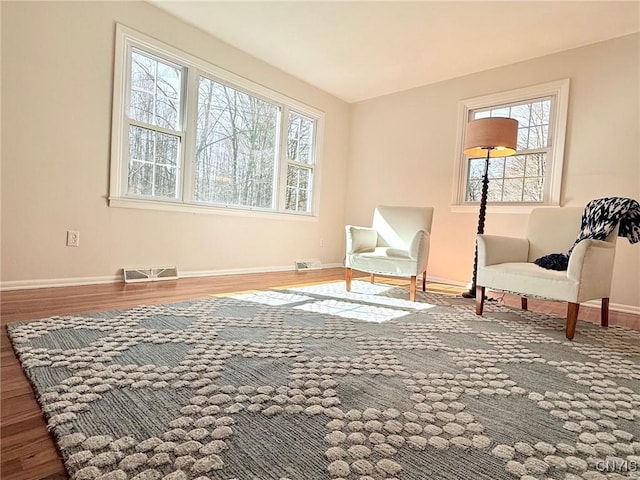 living area with baseboards, wood finished floors, visible vents, and a healthy amount of sunlight