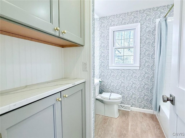 bathroom with wood finished floors, wallpapered walls, baseboards, toilet, and visible vents