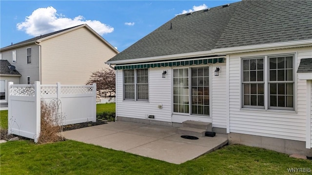 back of property with fence, a patio area, a lawn, and roof with shingles
