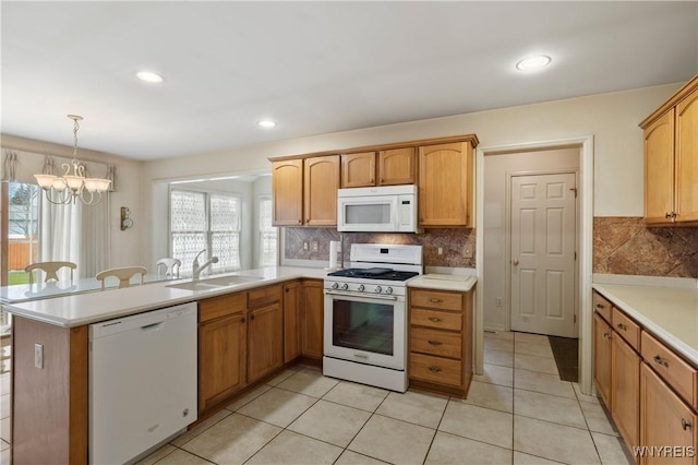 kitchen featuring a peninsula, a sink, a notable chandelier, white appliances, and light countertops