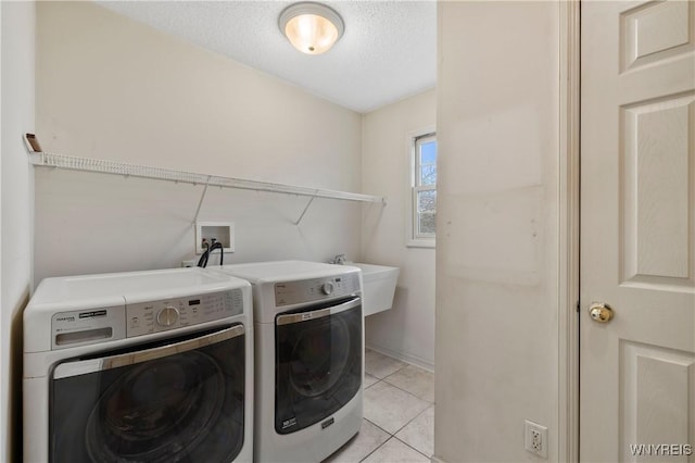 washroom with a sink, a textured ceiling, separate washer and dryer, laundry area, and light tile patterned floors