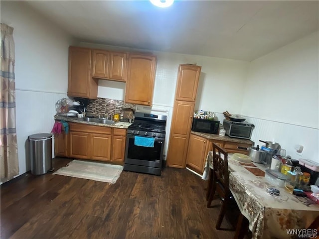 kitchen featuring stainless steel range with gas cooktop, a sink, wainscoting, black microwave, and dark wood-style flooring