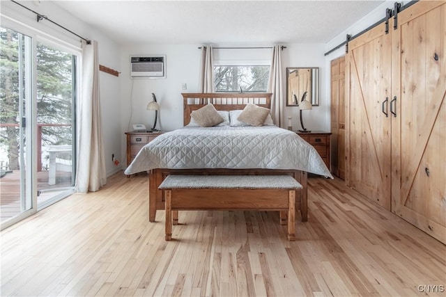 bedroom featuring a barn door, light wood finished floors, a wall mounted air conditioner, and access to exterior
