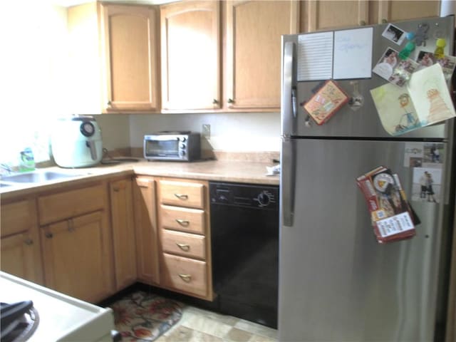kitchen featuring a toaster, light countertops, a sink, freestanding refrigerator, and black dishwasher