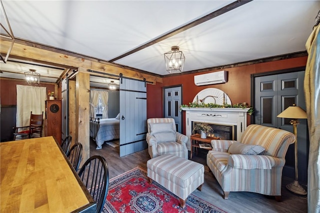 living room featuring a wall mounted air conditioner, a barn door, wood finished floors, a glass covered fireplace, and an inviting chandelier