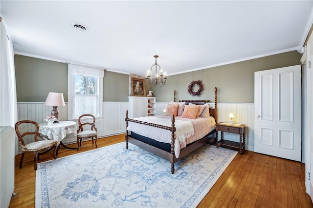 bedroom with radiator, wainscoting, visible vents, a chandelier, and wood finished floors