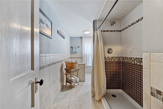full bathroom with tile walls, tile patterned floors, wainscoting, and tiled shower