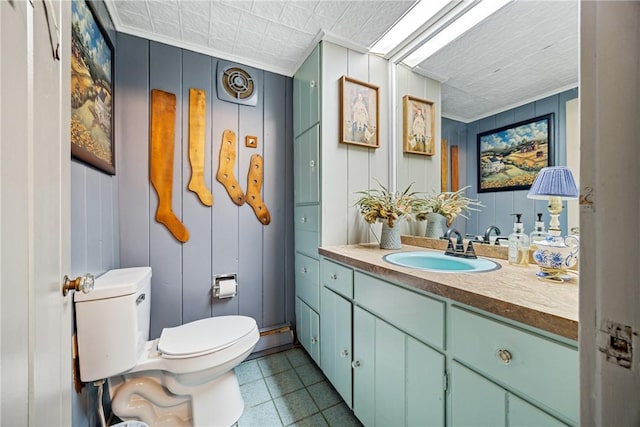 bathroom featuring toilet, crown molding, vanity, and a decorative wall