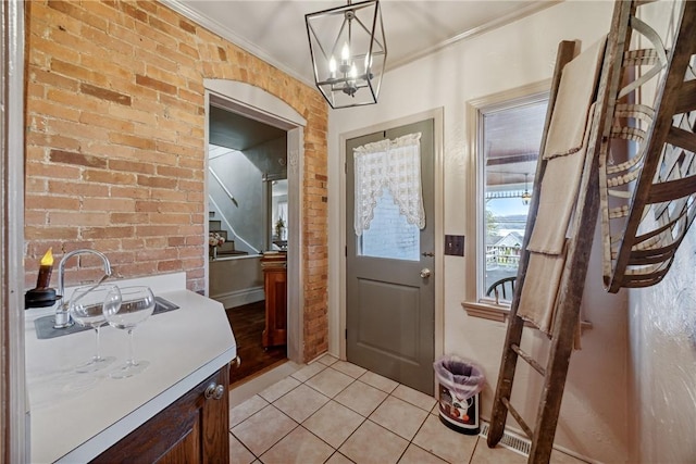 doorway to outside with a sink, light tile patterned flooring, an inviting chandelier, stairway, and crown molding